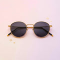 Round sunglasses with gold frame and black lenses on a pink background
