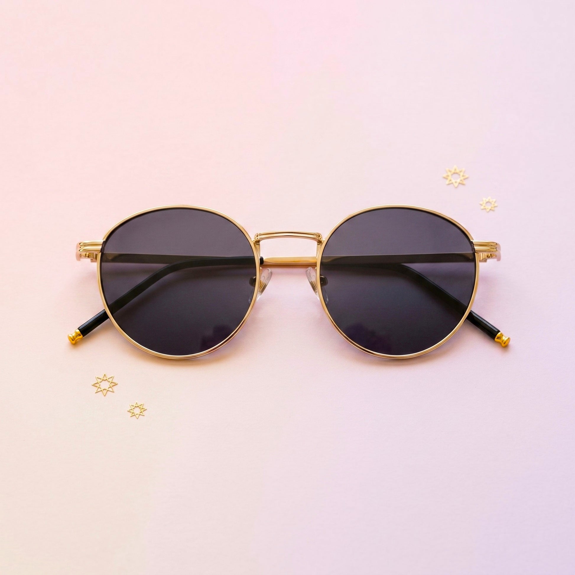 Round sunglasses with gold frame and black lenses on a pink background