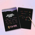 Two black spiral-bound books with colorful text on a light pink background