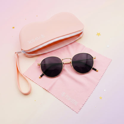 Round sunglasses with gold frame and dark lenses on a pink cloth with a pink case in the background.