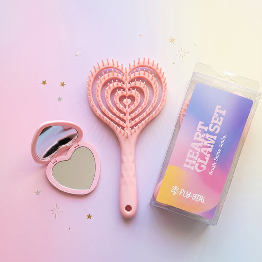 Heart-shaped hairbrush and compact mirror with packaging on a light pink background