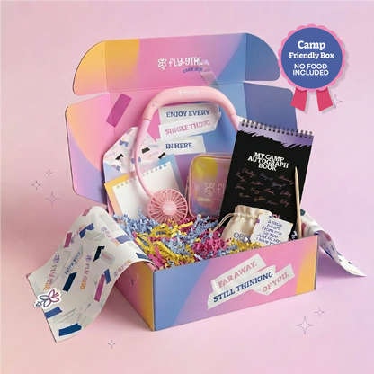 A colorful open gift box labeled 'Fly Girl' filled with assorted cute items including a pink fan, notebook, pouch, and small accessories, set against a soft pink background with a 'Camp Friendly Box No Food Included' badge.