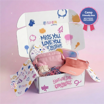 An open Fly Girl Campfire themed cardboard gift box filled with pink accessories, including a pink pouch, a peach visor, and a small plush toy, set against a soft pink background with a 'Camp Friendly Box' badge.