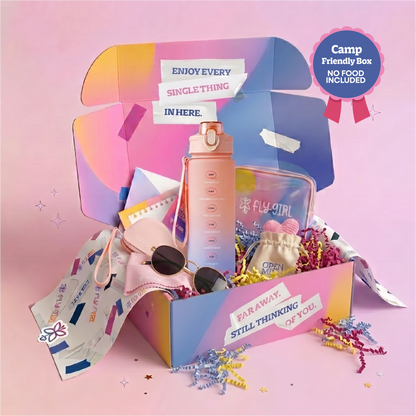 A colorful open gift box filled with travel-themed items on a pink background. Visible contents include a tall pink water bottle, a clear zip pouch labeled FLY GIRL, a small beige pouch, sunglasses, and paper accessories.