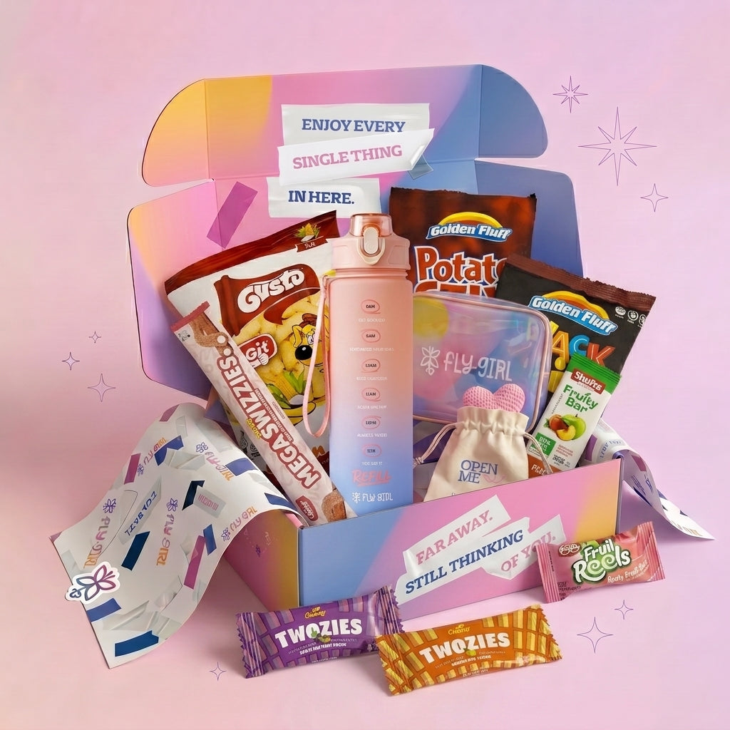 A curated gift box filled with assorted snacks, candy, and a pink water bottle, arranged on a pastel pink background with decorative sparkles. Visible brands include Golden Flud, GYRO, Twozies, and Fly Girl.