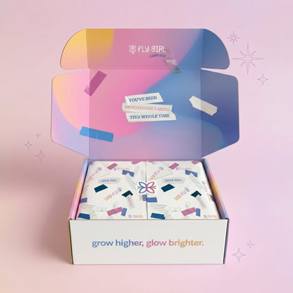 Open box with colorful packaging and 'Fly Girl' branding on a pink background
